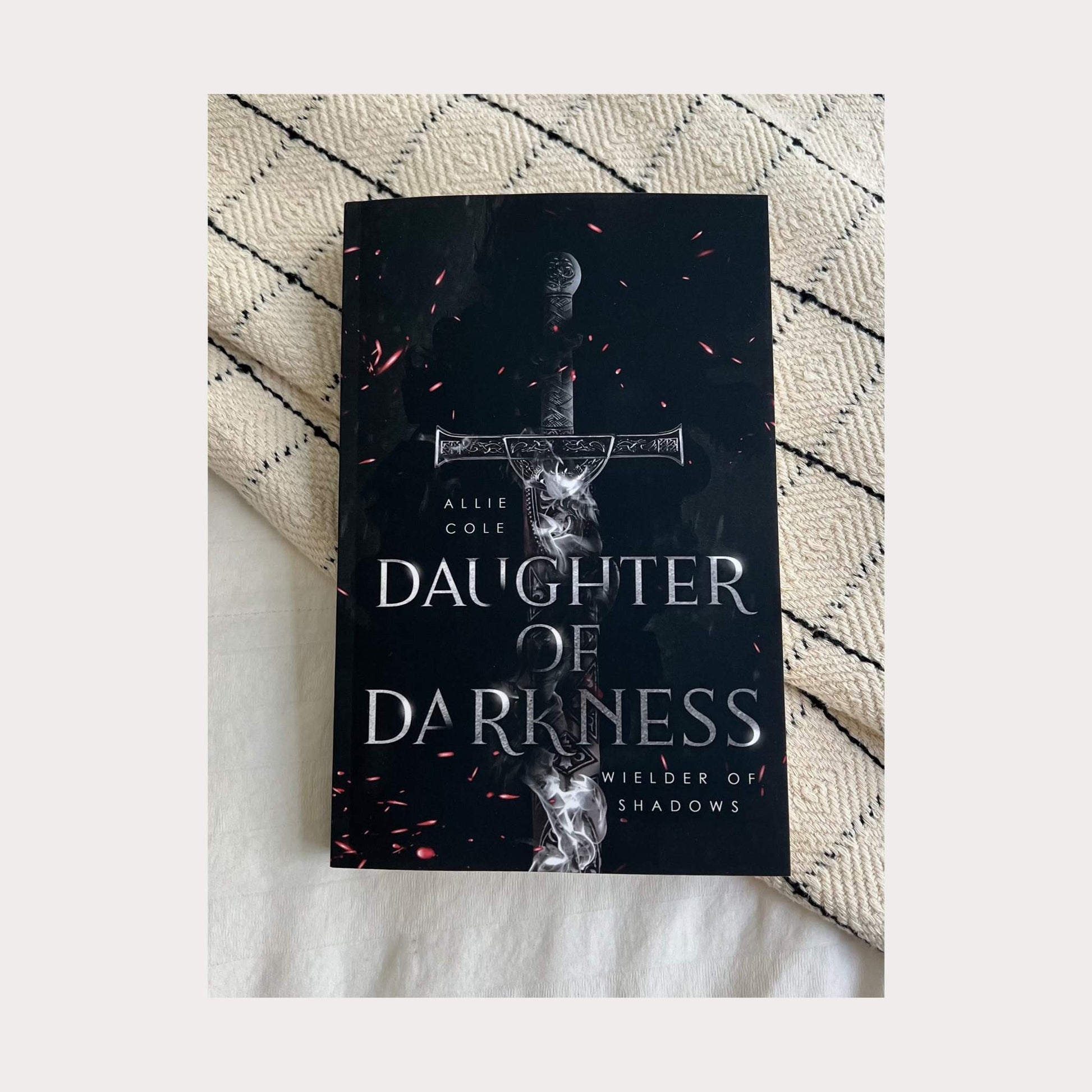 A paperback copy of Daughter of Darkness: Wielder of Shadows by Allie Cole—an enemies-to-lovers, slow-burn fantasy romance with fated mates, revenge, and forbidden love—set against a textured beige and black blanket. Perfect for fans of dark fantasy and epic romance.