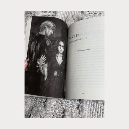 A reader holding an open copy of Daughter of Darkness Prince of Bloodshed by Allie Cole, showing a black and white character illustration on the left page featuring a dark-haired woman and a pale-haired man standing together in an intense scene. The right page displays the title Part II The Ghost of Nyths along with the quote This is my game now