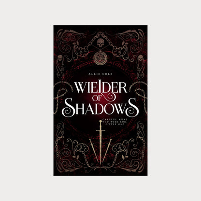 Hardcover edition of Wielder of Shadows by Allie Cole, a dark fantasy romance novel. The cover features gothic filigree, chains, skulls, and a glowing red background, with a silver sword at the center. The tagline reads Careful what you wish for, little one